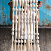 Person holding a macrame wall hanging against a textured blue and brown wall.