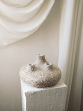 Textured ceramic vase on a white pedestal with draped fabric in the background