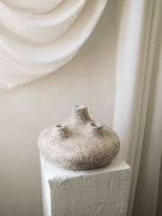 Textured ceramic vase on a white pedestal with draped fabric in the background