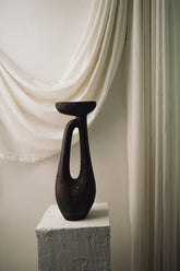 Black vase on a white pedestal against a draped white curtain