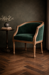 Green velvet chair with wooden frame in a dimly lit room
