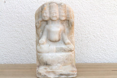 Marble sculpture of a seated figure on a wooden surface with a white textured wall background