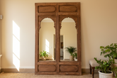 Large wooden mirror with arched designs on a beige wall.