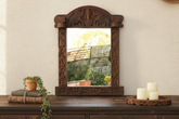 Decorative wooden mirror with carvings on a wooden surface with candles and plants.