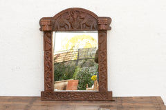 Carved wooden mirror with elephant design on a white wall