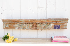Decorative wooden mantel with carvings on a white wall, accompanied by books and flowers.