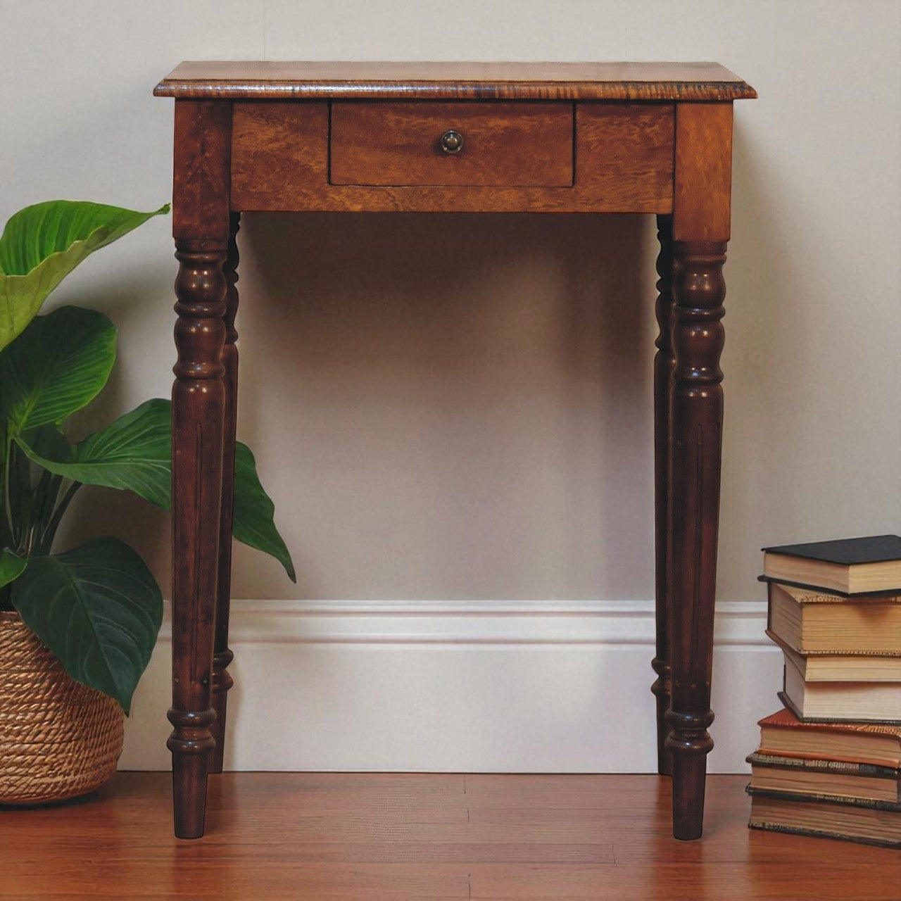 Wooden side table with a drawer next to a stack of books and a plant on a wooden floor.