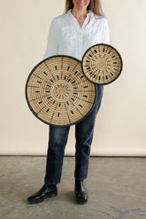 Person holding two large circular wooden items with intricate designs against a neutral background