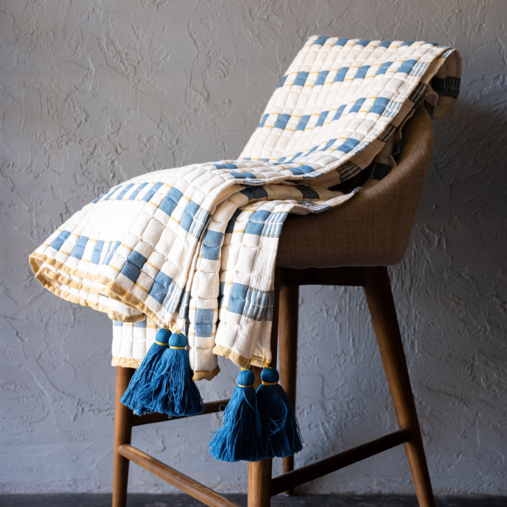 Indra handwoven cotton Sujani throw in warm cream, indigo blue, and muted mustard with oversized blue corner tassels