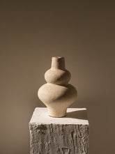 Stacked stone vases on a textured pedestal against a plain background