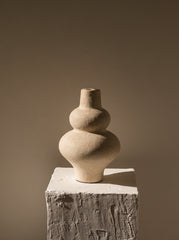 Stacked stone vases on a textured pedestal against a plain background