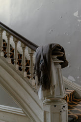 Brown blanket draped over a wooden stair railing in an old building.