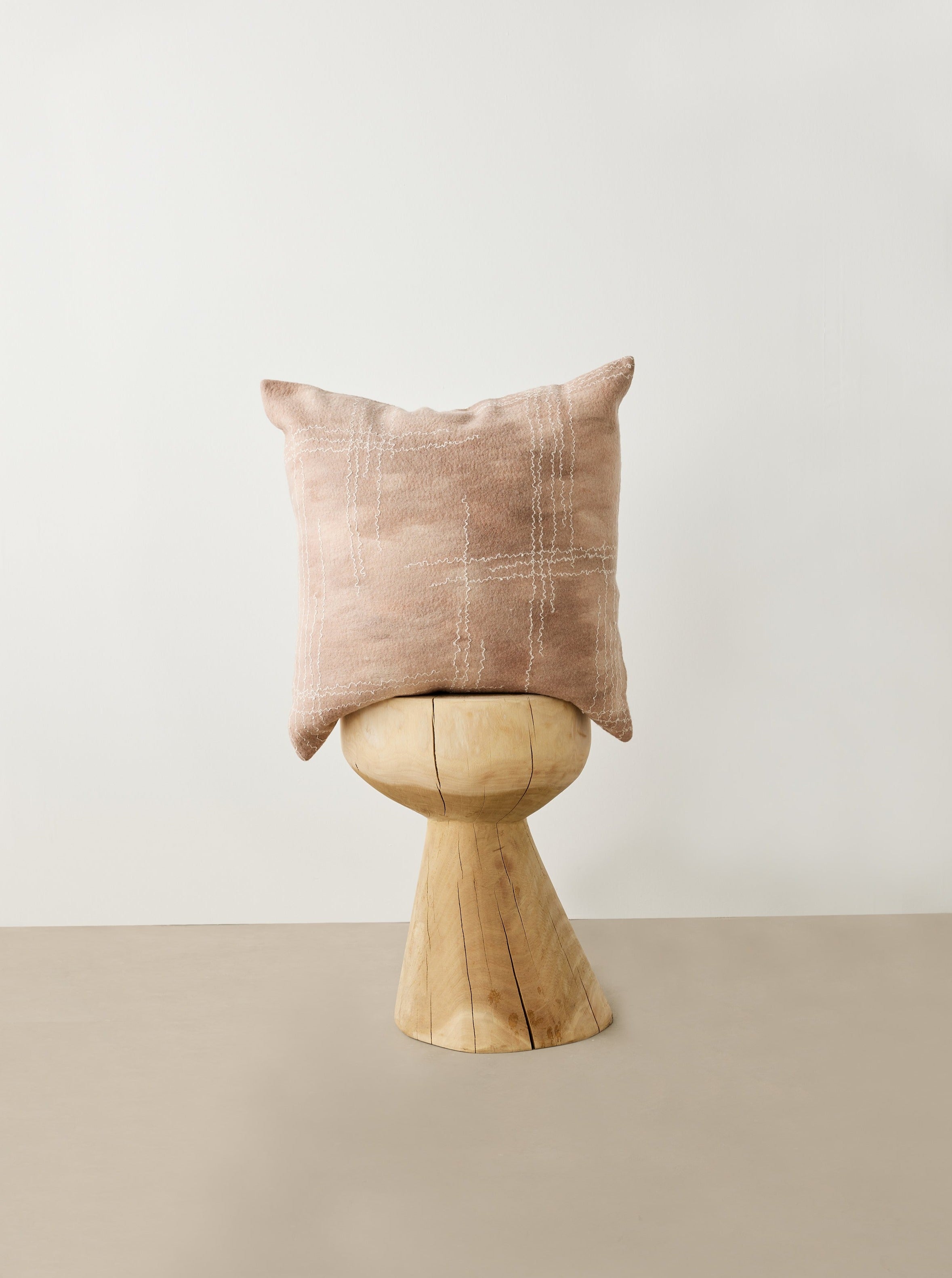 Pink pillow on a wooden stool against a white wall