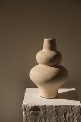 Stacked stone vases on a textured platform against a brown background