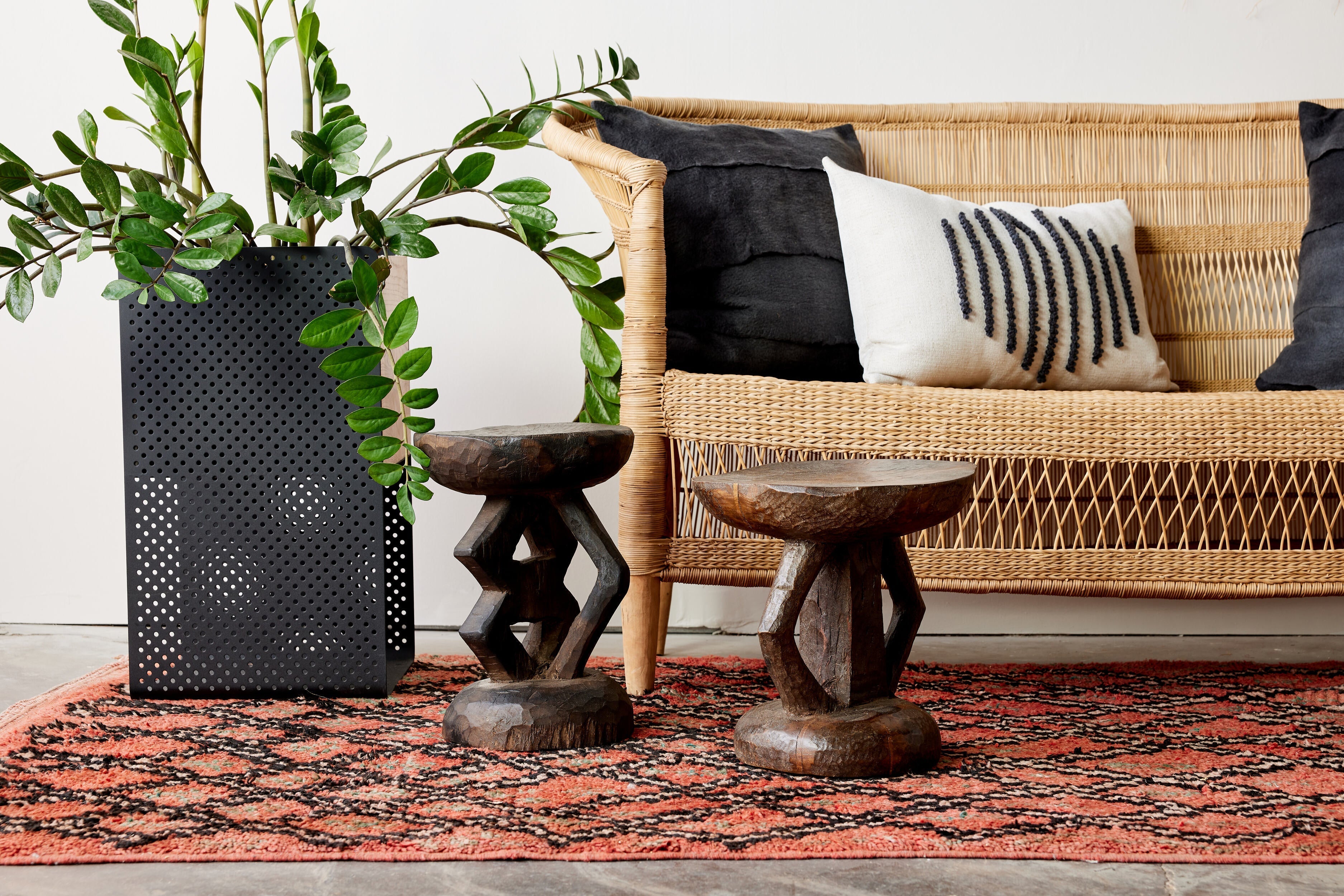 Wicker sofa with decorative pillows, plant, and small tables in a living room setting.