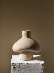 Stoneware vase on a textured pedestal against a beige background