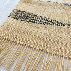 Woven mat with fringes and a black stripe on a light background