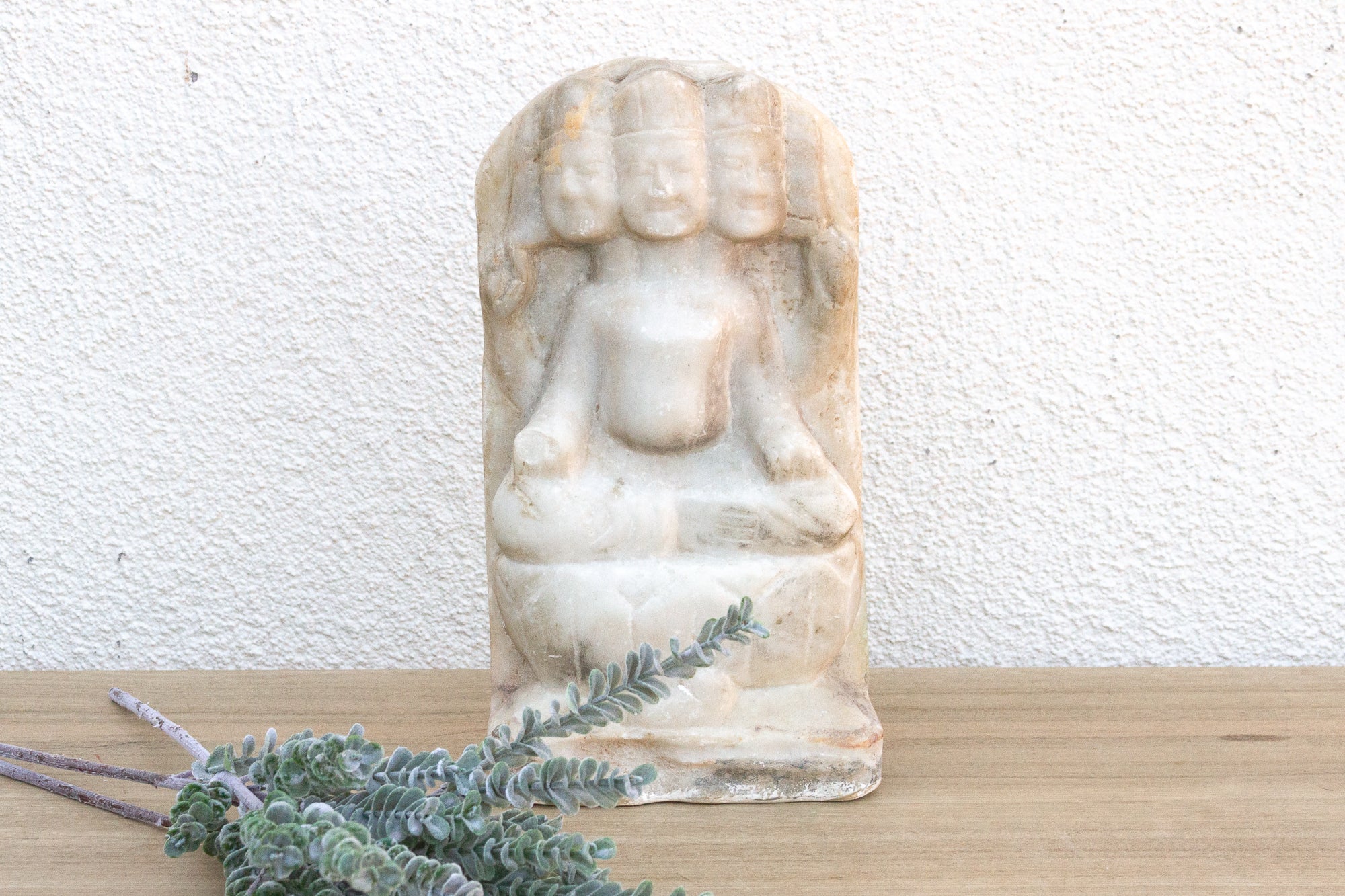 White marble statue of a seated figure on a wooden surface with a white textured wall background