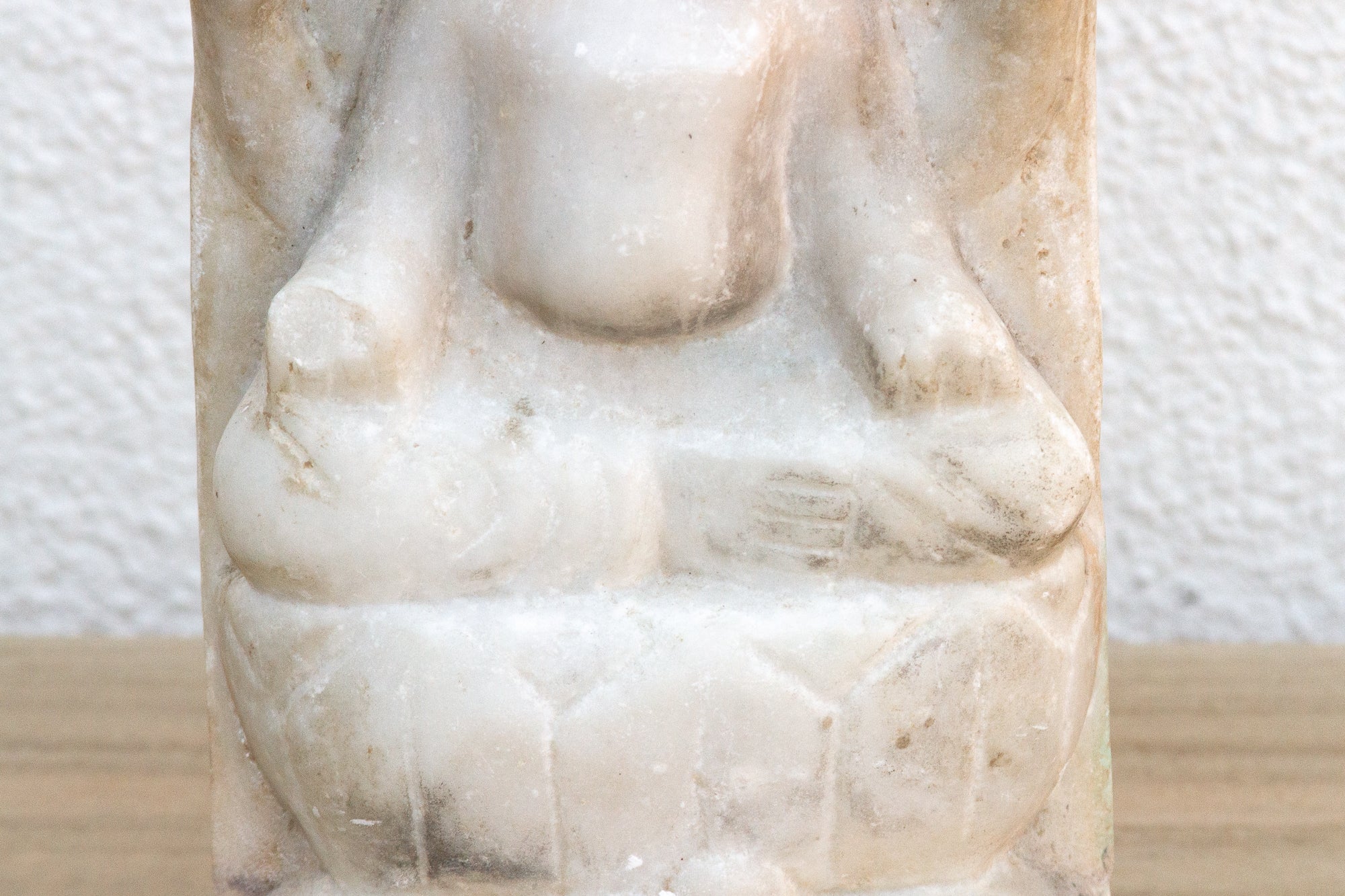 White stone sculpture of a seated figure on a textured white background