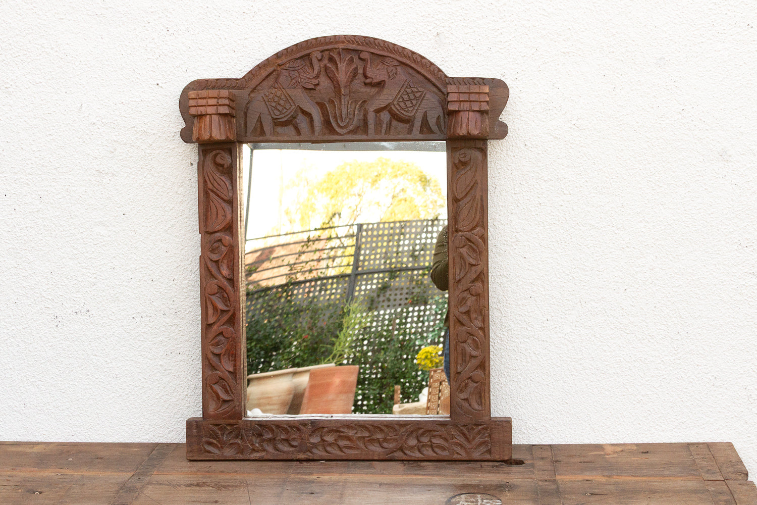 Carved wooden mirror with elephant design on a white wall