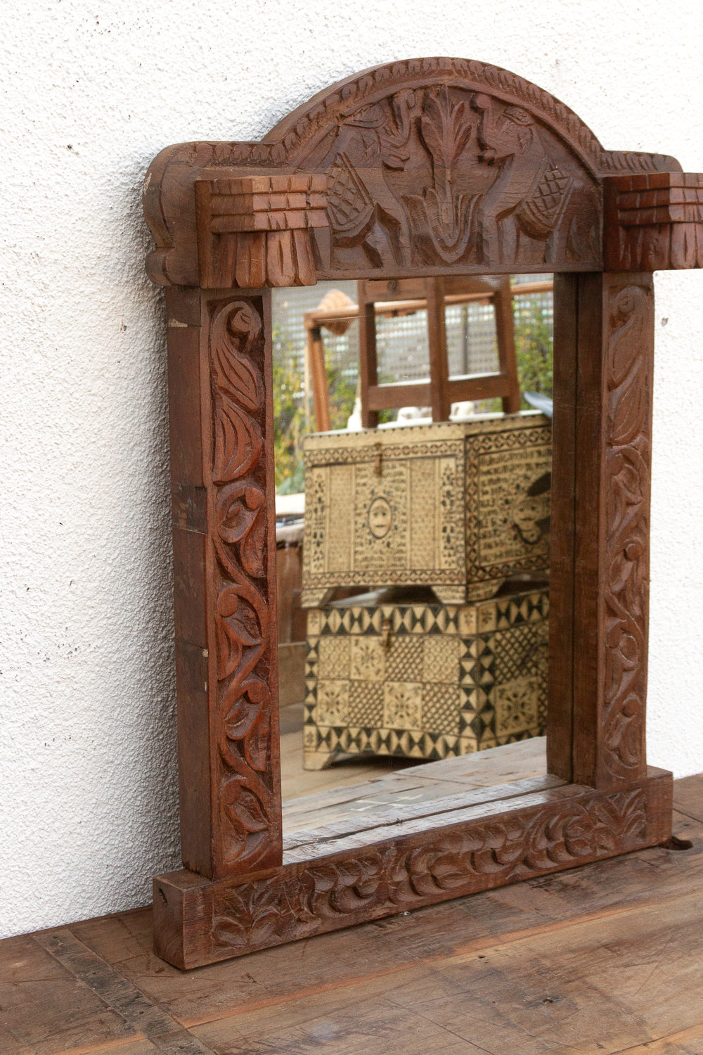 Carved wooden mirror with intricate designs on a white wall.