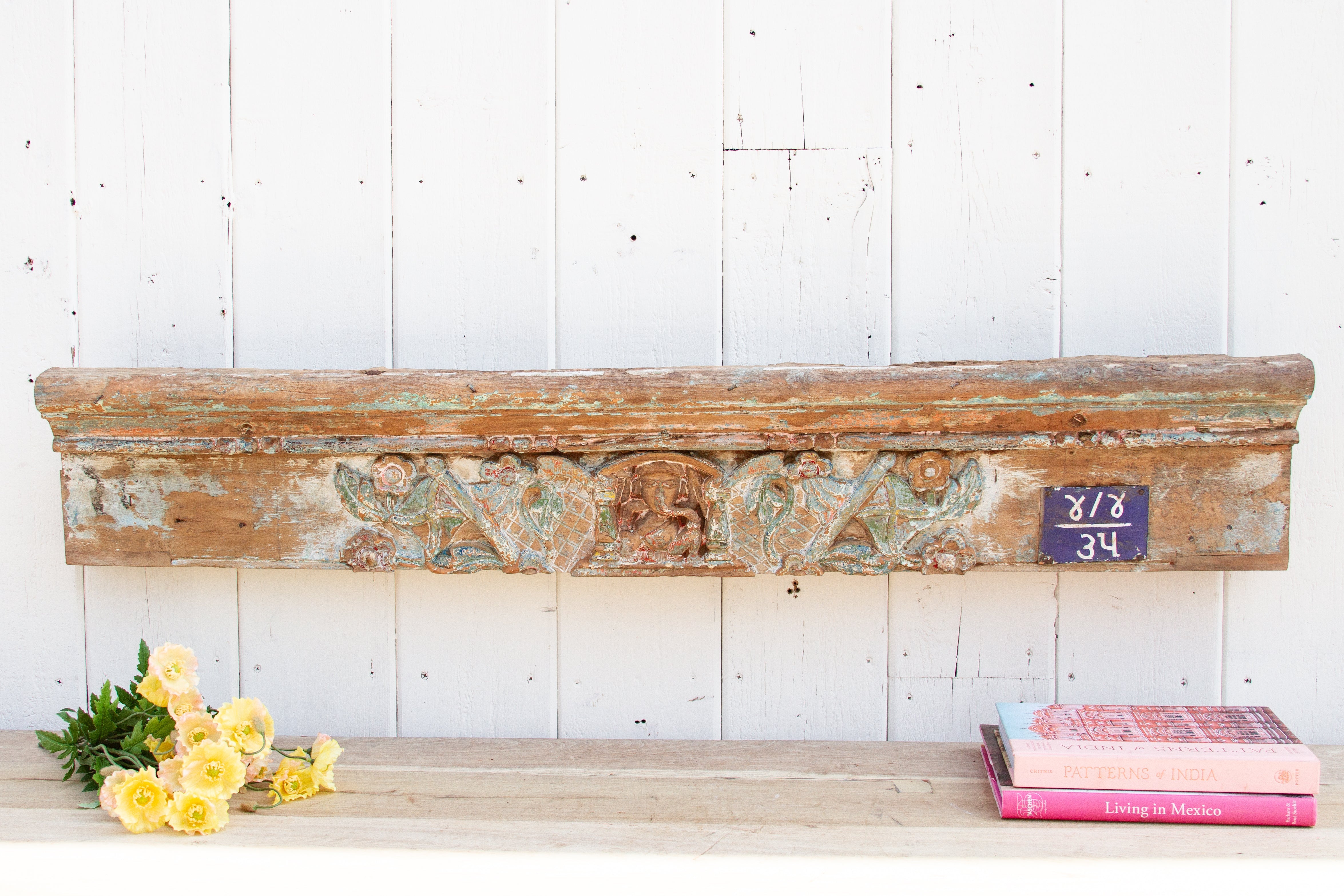 Decorative wooden mantel with carvings on a white wall, accompanied by books and flowers.