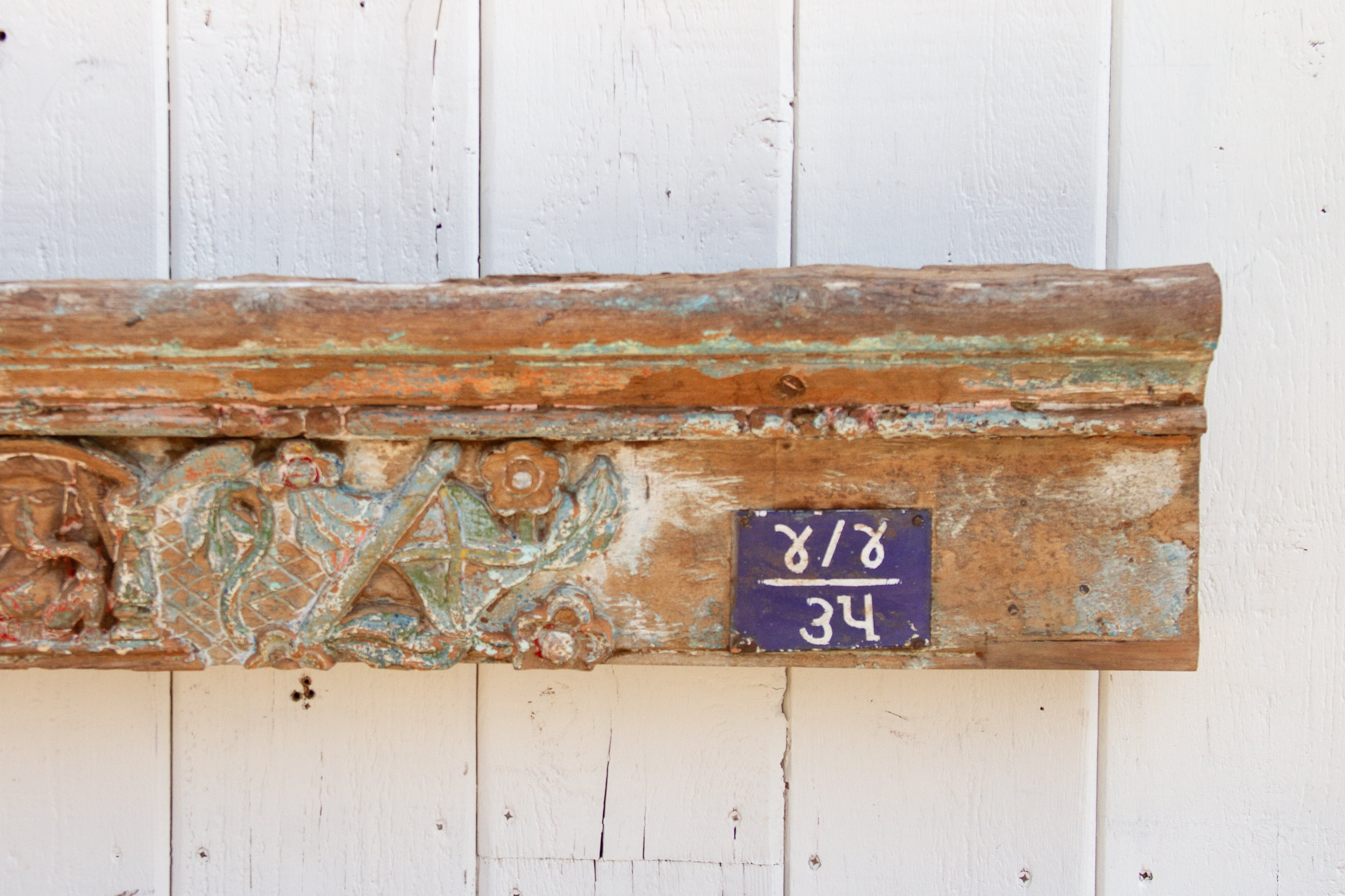 Decorative wooden panel with intricate carvings and a purple label on a white background