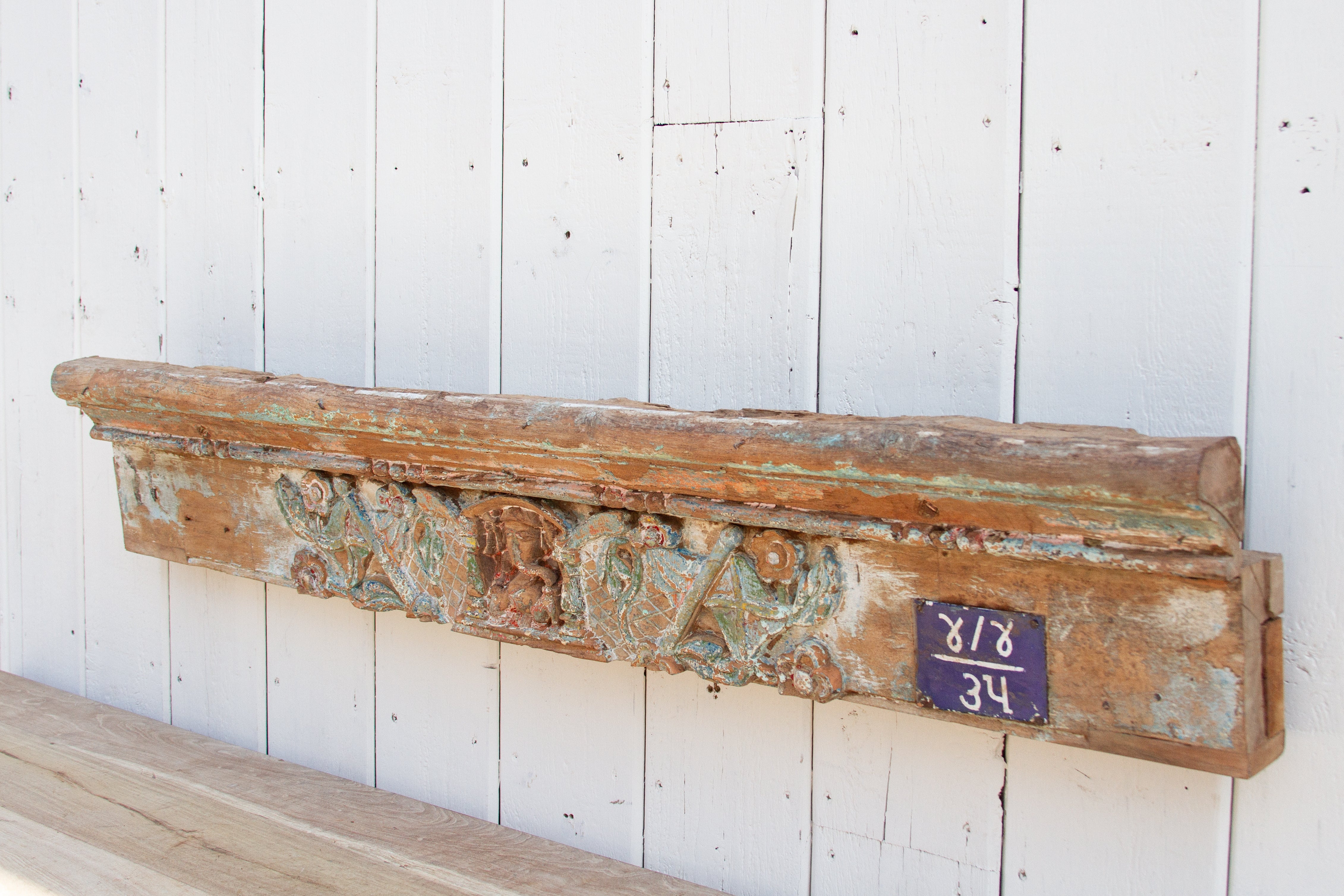 Vintage wooden shelf with decorative carvings against a white wooden panel background