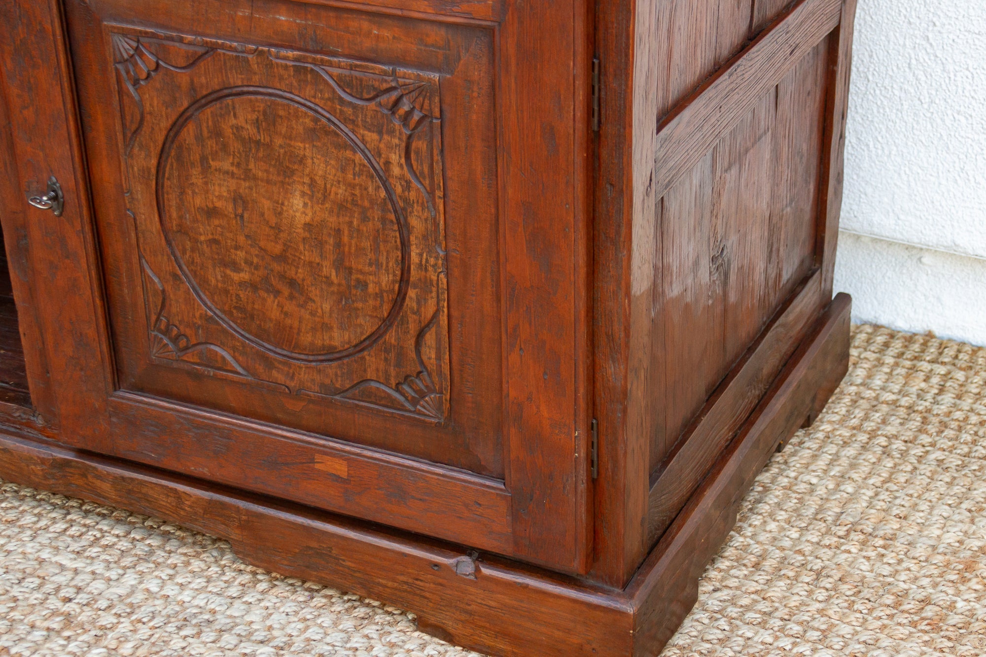 Close-up of a wooden cabinet with intricate carvings on a textured floor.