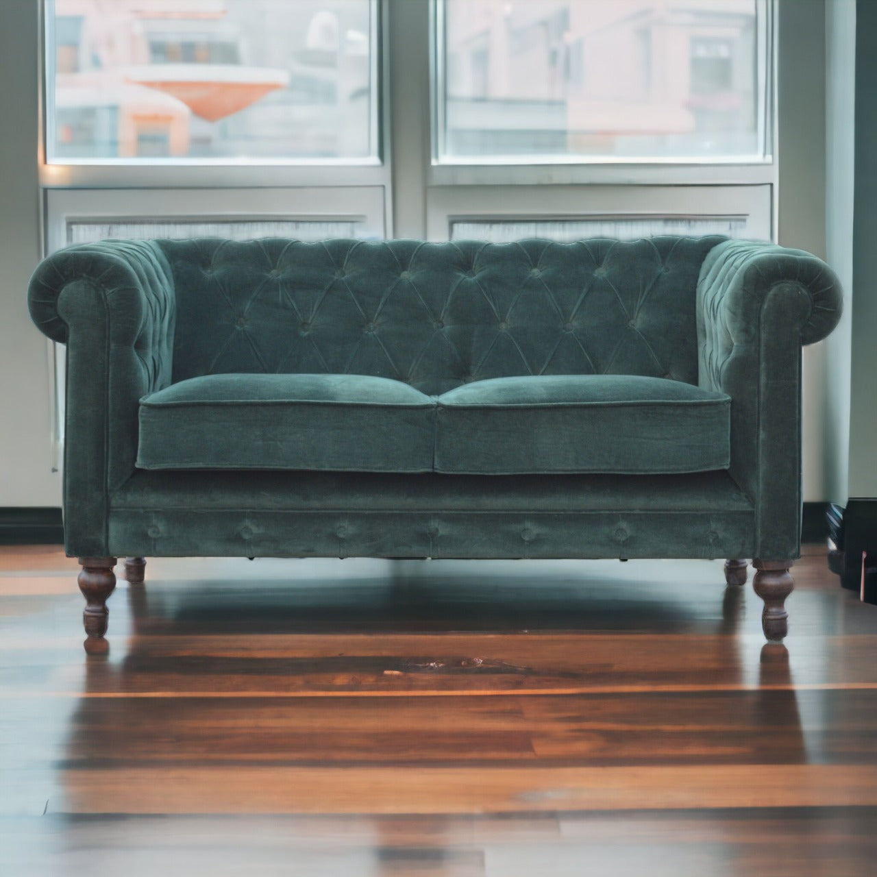 Green velvet sofa in a room with large windows and wooden floor.