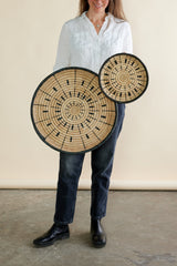Person holding two large circular wooden items with intricate designs against a neutral background