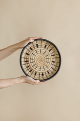Woven basket with spiral pattern held by a person against a beige background