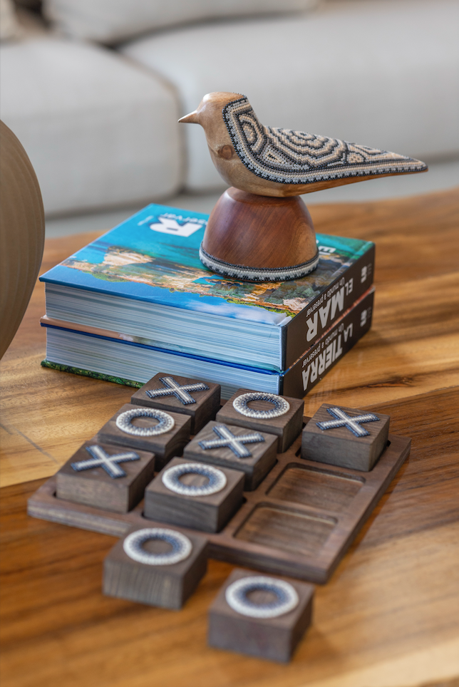 Wooden tic-tac-toe game set on a table with books and a decorative bird figurine in the background.