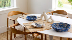 Dining table set with chairs, plates, and decorative items in a bright room.