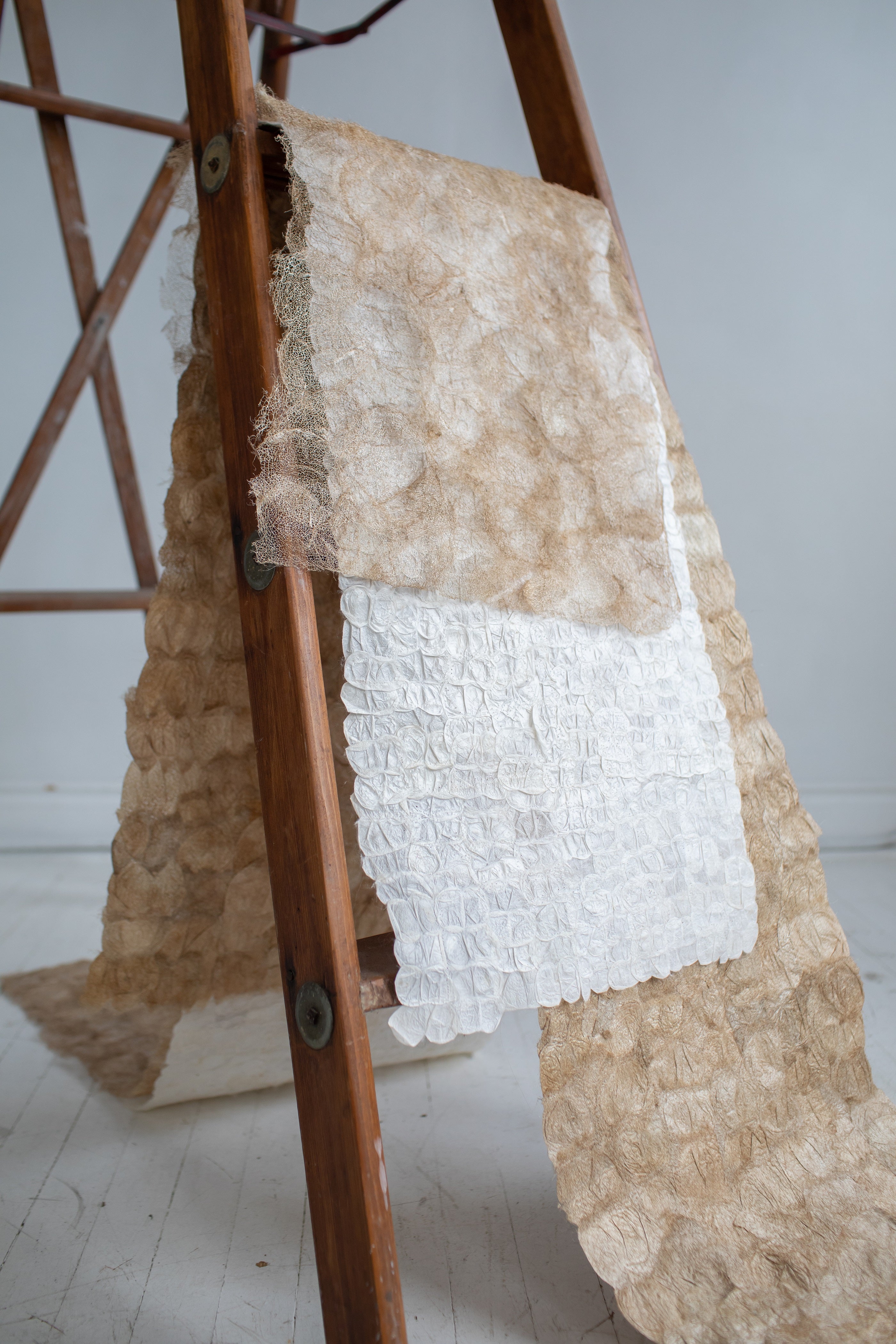 Textured fabric samples on a wooden ladder against a white wall.