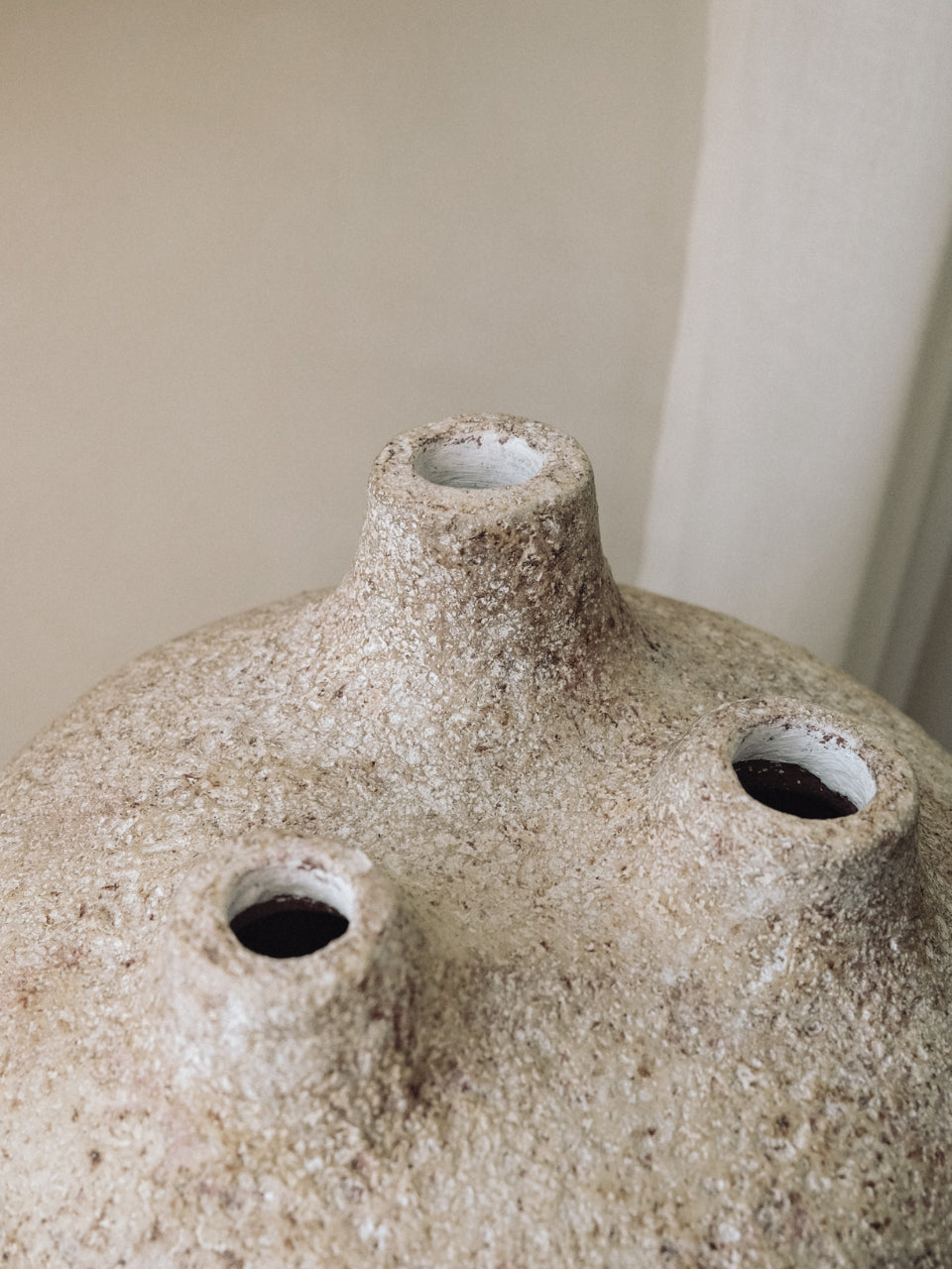 Textured ceramic vase with three holes against a neutral background