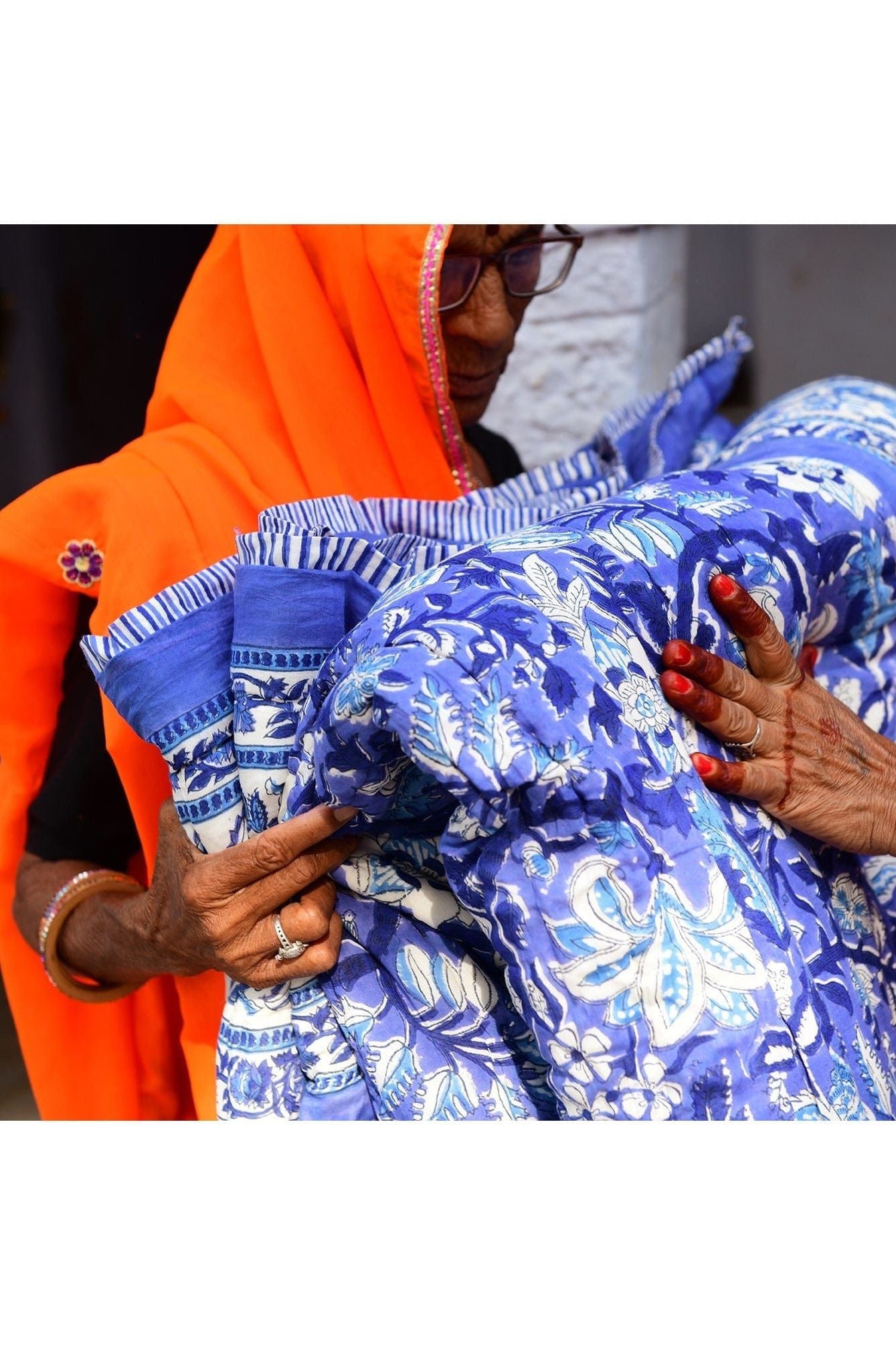 Person holding a blue patterned fabric with an orange garment in the background