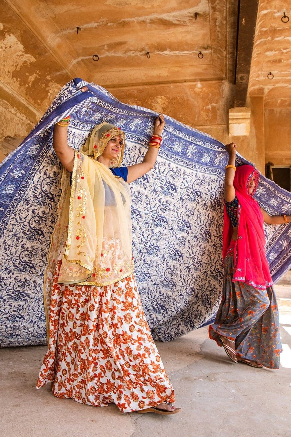 Two women holding a large blue and white patterned fabric in an indoor setting.