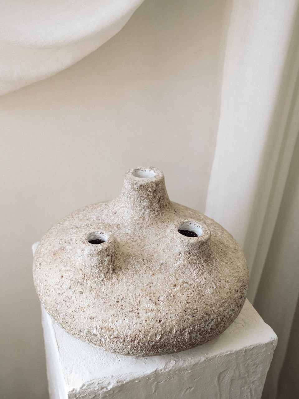 Textured ceramic vase on a white pedestal against a neutral background