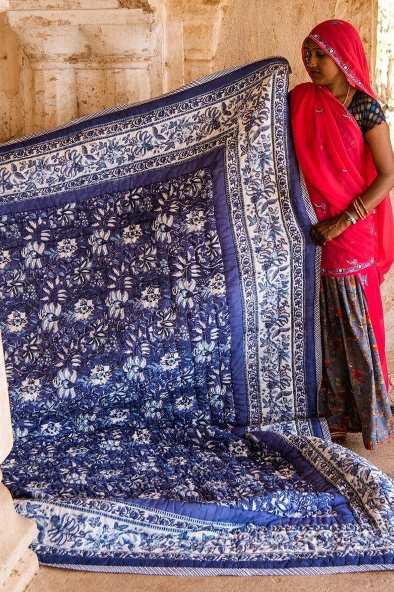Woman holding a large blue and white patterned fabric in an outdoor setting.