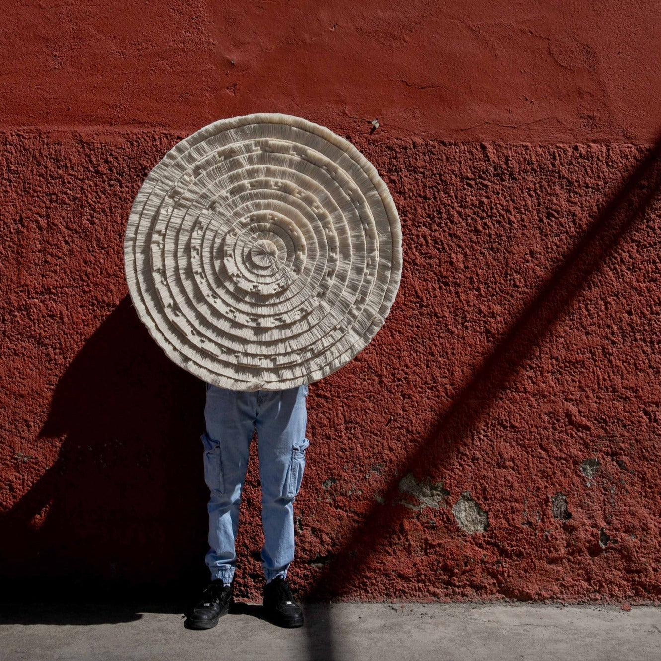 Person holding a large circular object against a red wall