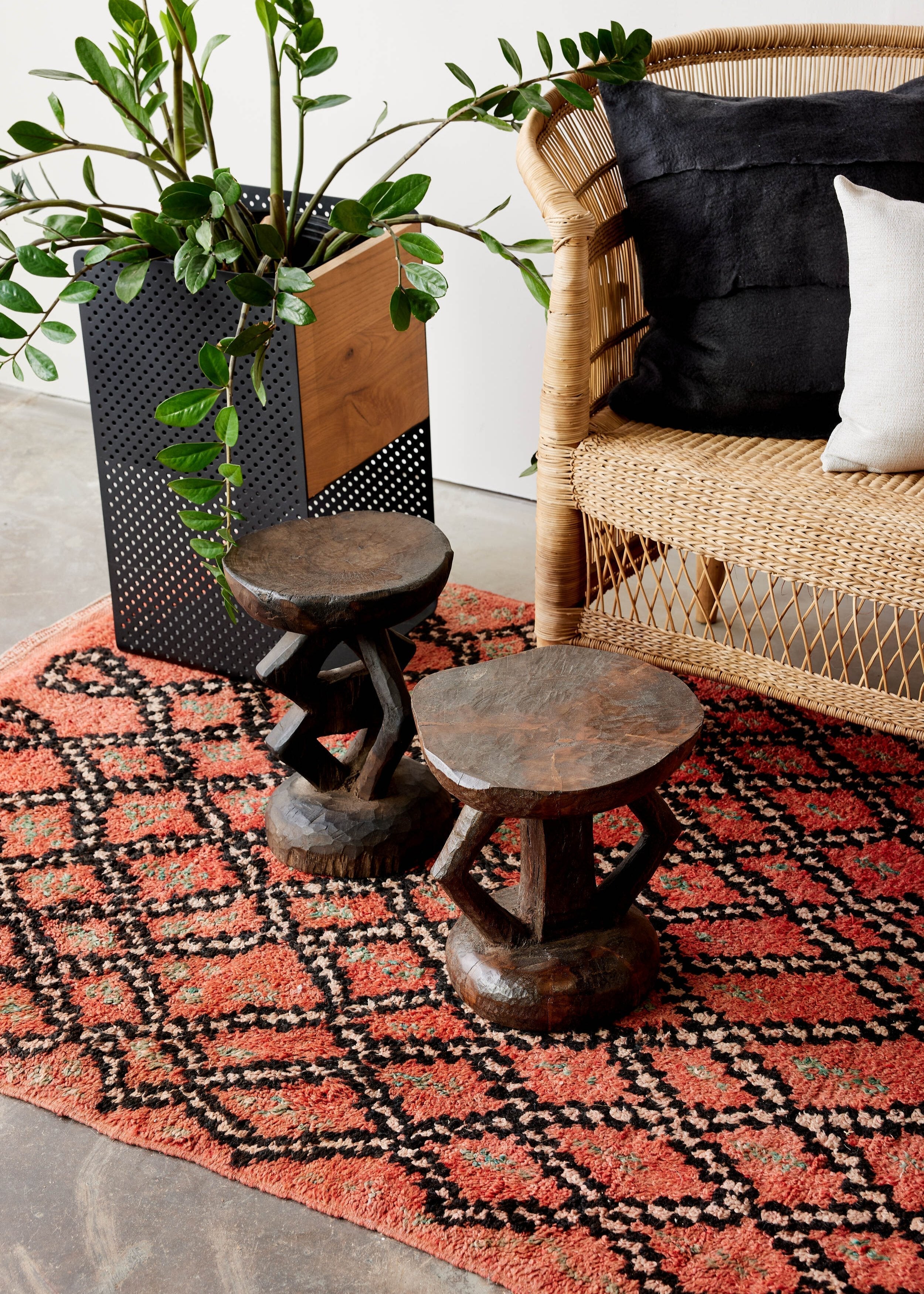 Wicker chair with black and white cushions, wooden stools, and a patterned rug in a room.